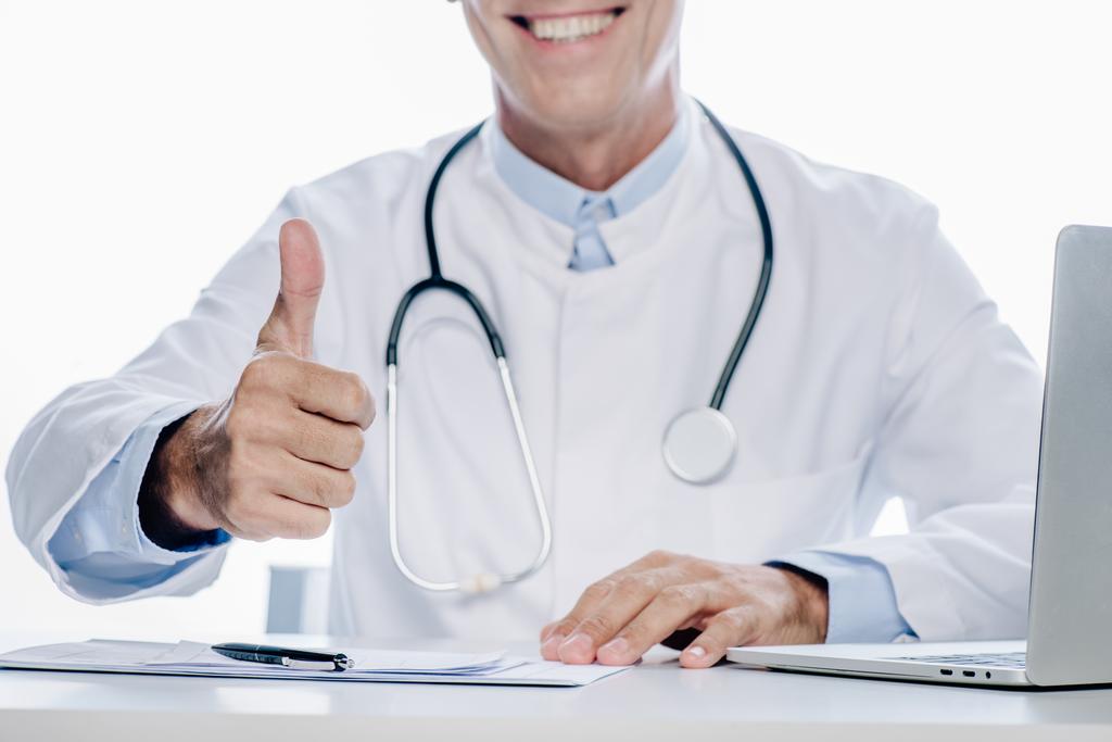 обрезанный вид доктора в белом халате улыбается и показывает большой палец вверх изолированы на белом
  - Фото, изображение