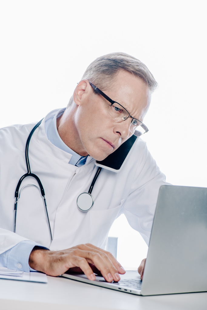 médico bonito em casaco branco falando no smartphone e usando laptop isolado no branco
 - Foto, Imagem