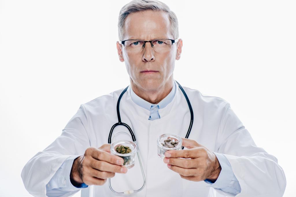 pohledný doktor v bílém plášti, který drží lékařskou marihuonu a tablety izolované na bílém - Fotografie, Obrázek