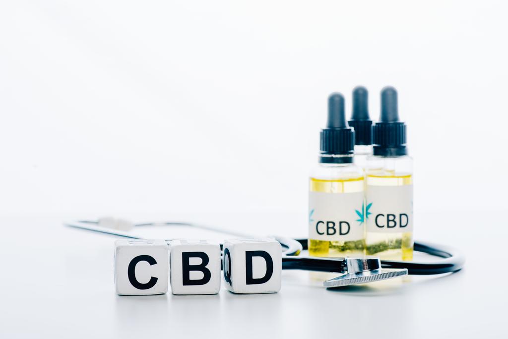 aceite de cannabis en botellas con letras cbd, cubos y estetoscopio sobre fondo blanco
  - Foto, imagen