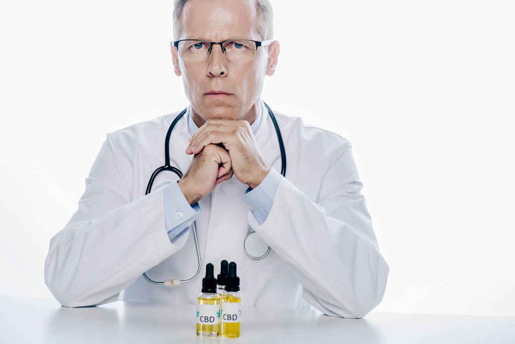 handsome doctor in white coat with cbd on table isolated on white  - Photo, Image