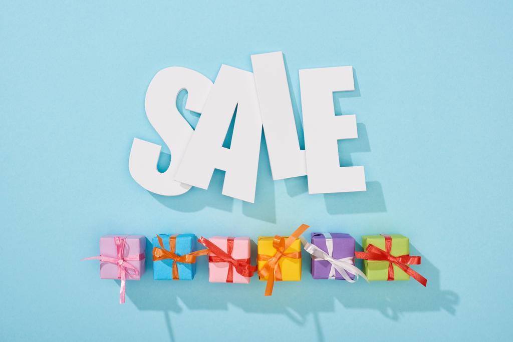 Top uitzicht van witte verkoop woord boven feestelijke verpakt presenteert op blauwe achtergrond - Foto, afbeelding