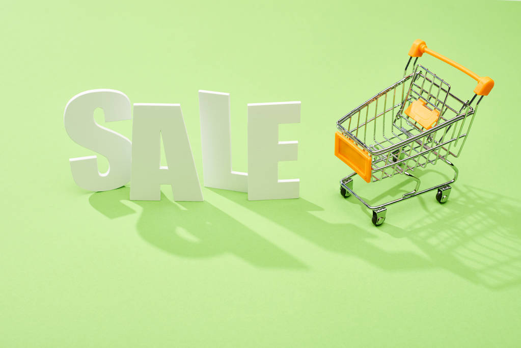 white sale lettering near decorative shopping cart on green background - Photo, Image