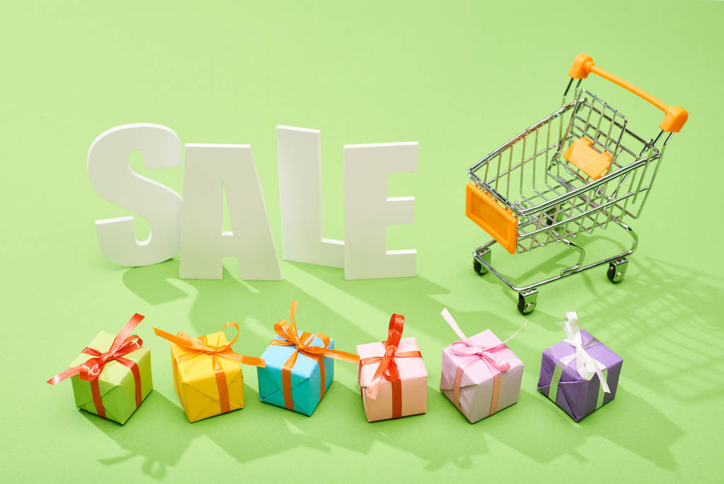 white sale lettering near decorative gift boxes and shopping cart on green background - Photo, Image
