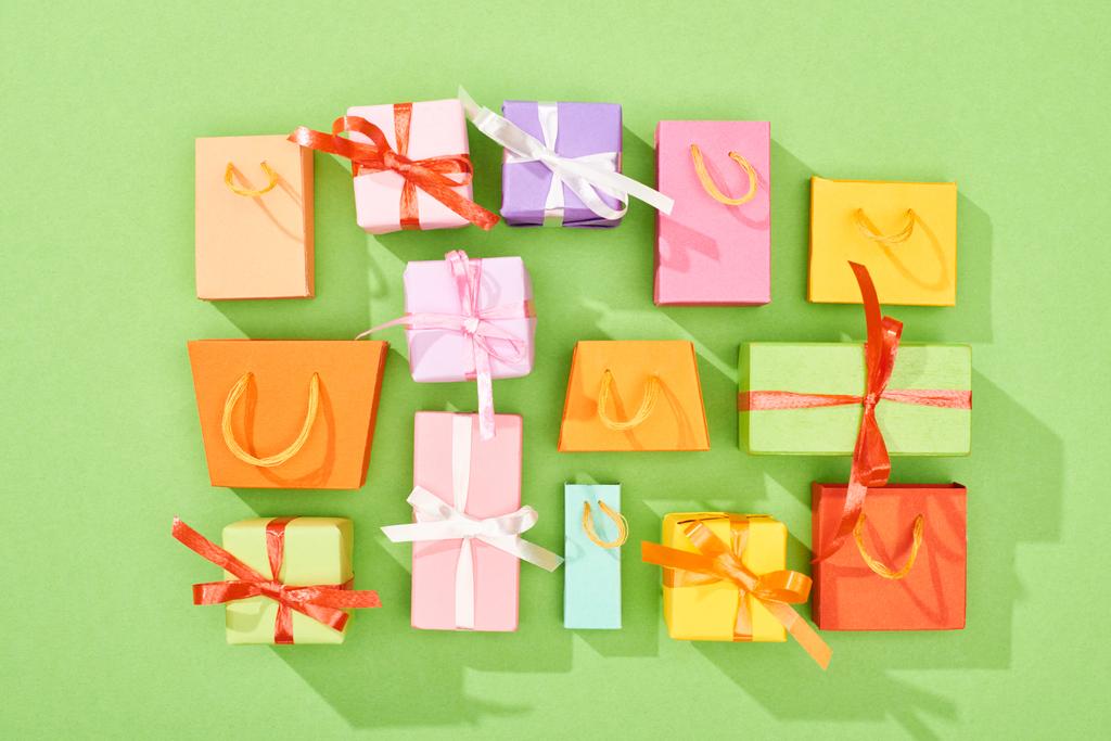 Draufsicht auf dekorative Geschenkboxen und Einkaufstaschen auf grünem Hintergrund - Foto, Bild