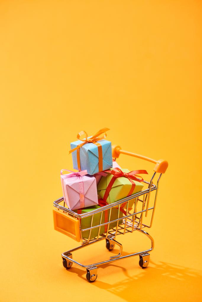 διακοσμητικό καλάθι αγορών με δώρα σε φωτεινό πορτοκαλί φόντο - Φωτογραφία, εικόνα