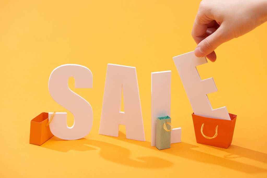 обрезанный вид человека, держащего письмо от белой распродажи буквы возле торговых мешков на оранжевом фоне
 - Фото, изображение