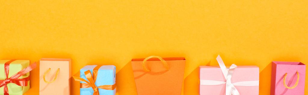 panoramatický záběr nákupních sáčků a sváteční zabalené dary na zářivě oranžovém pozadí - Fotografie, Obrázek