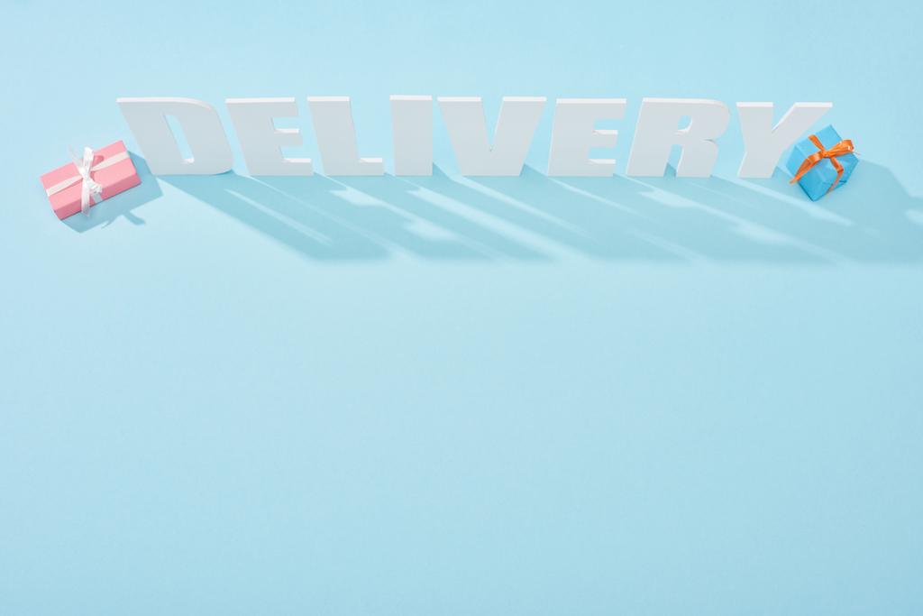 верхний вид белой надписи доставки с тенями возле подарочных коробок на синем фоне
 - Фото, изображение