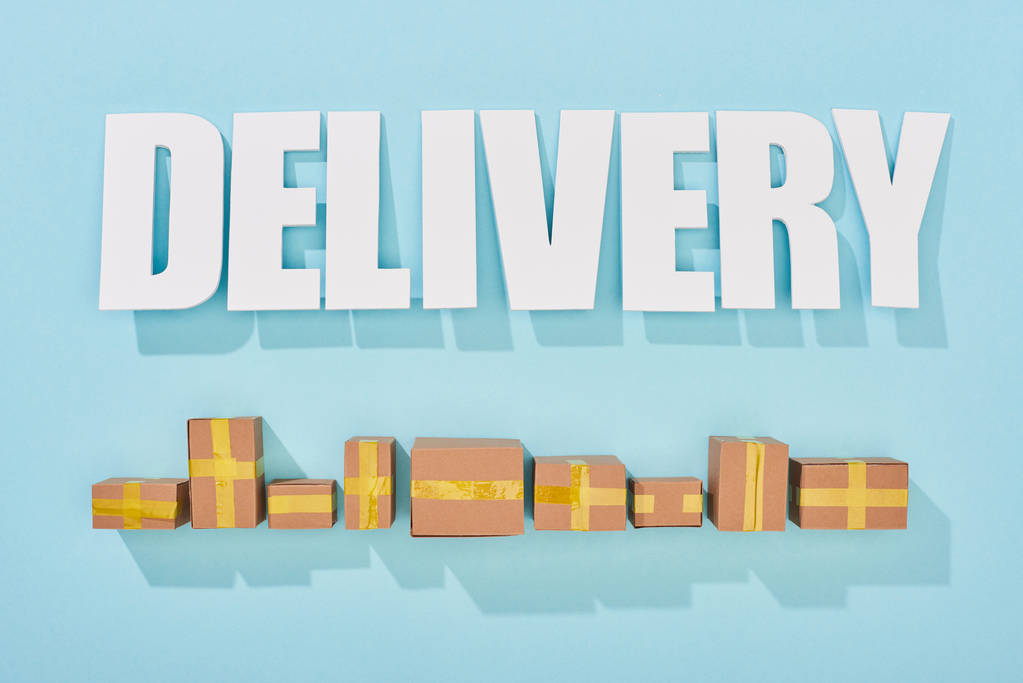 delivery inscription with shadows near closed cardboard boxes on blue background with copy space - Photo, Image