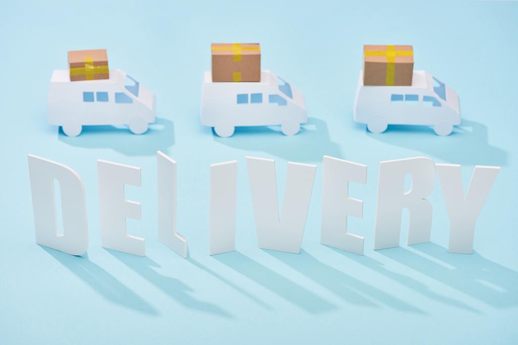 mavi arka plan üzerinde karton kutular ile mini kamyonlar altında beyaz teslimat yazıt - Fotoğraf, Görsel