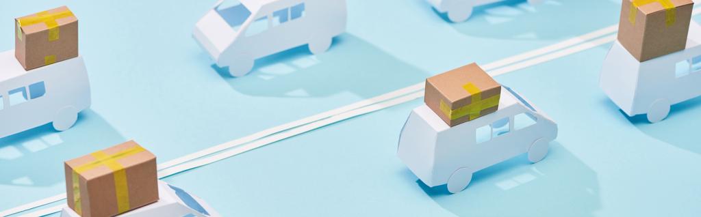 panoramic shot of miniature trucks with cardboard parcels on blue background with double line - Photo, Image