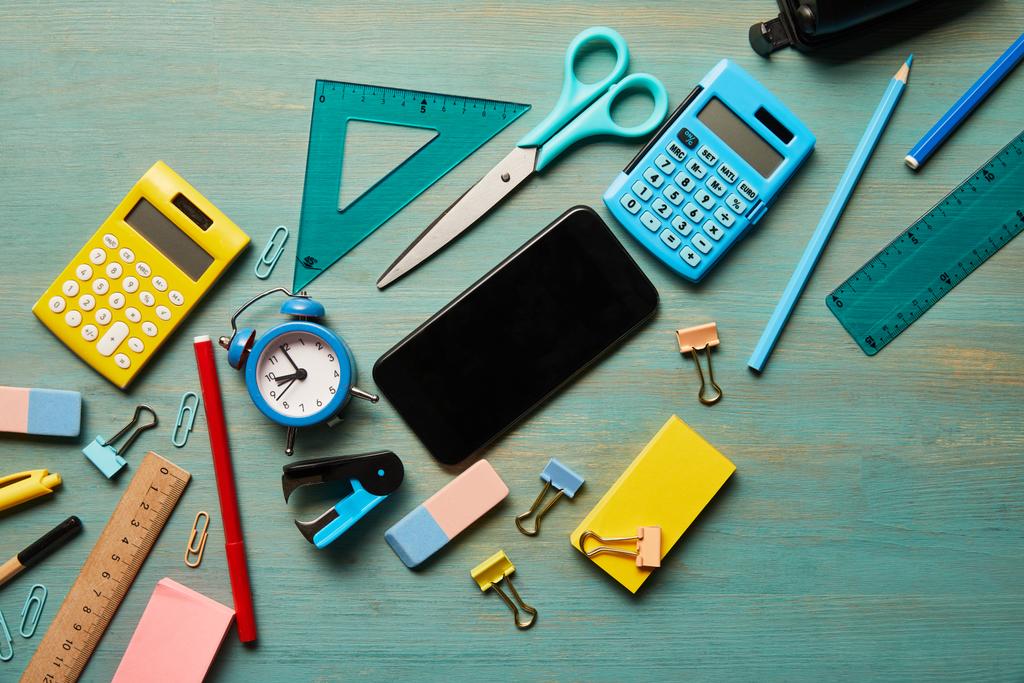 top view of smartphone with blank screen near school supplies at turquoise wooden table - Photo, Image