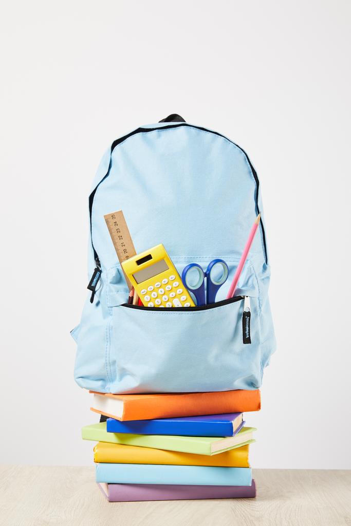 mochila azul con suministros en bolsillo en libros aislados en blanco
 - Foto, imagen