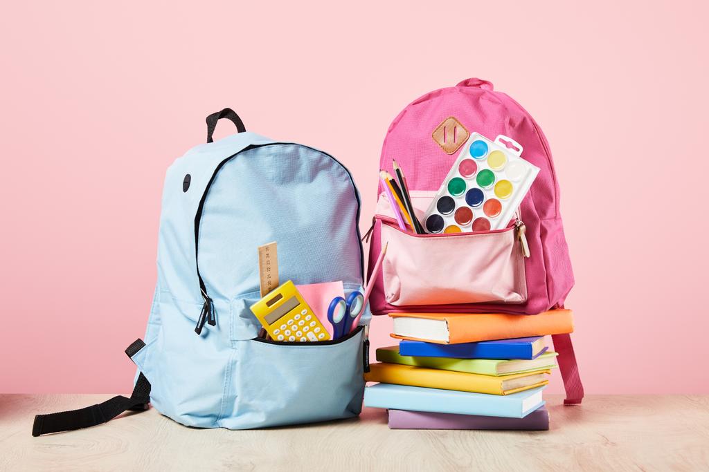 pembe izole kitapların yakınında okul malzemeleri ile mavi ve pembe sırt çantaları - Fotoğraf, Görsel