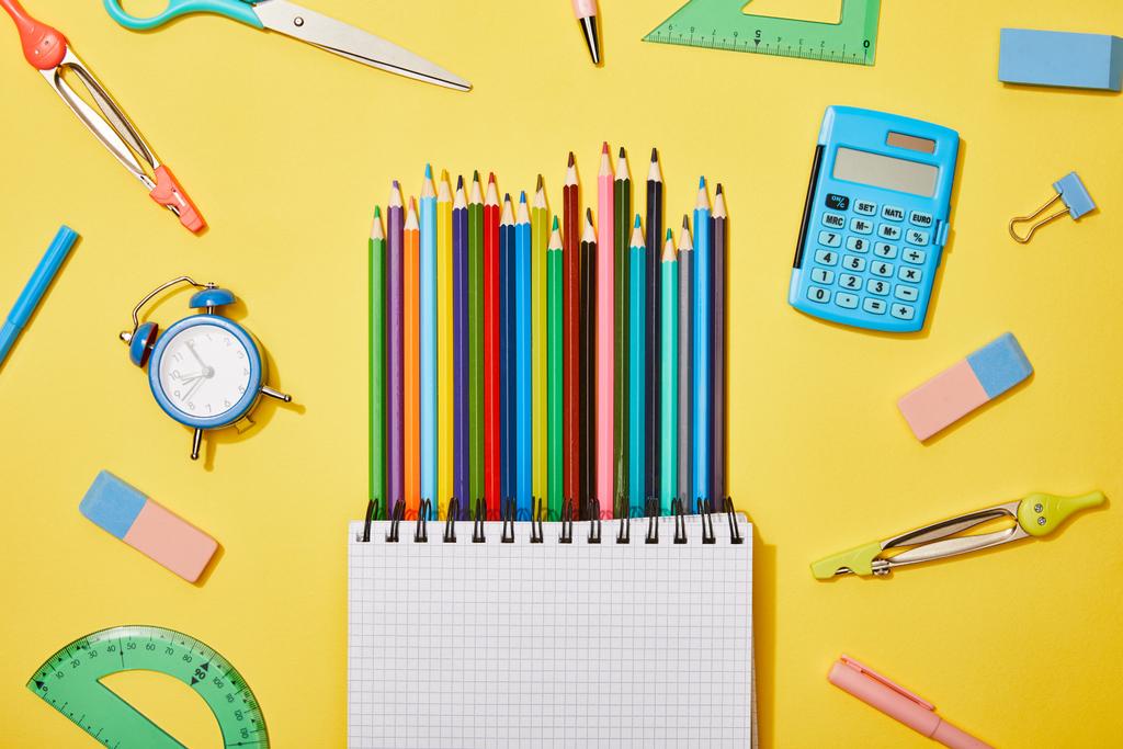 vista dall'alto di matite colorate notebook in bianco tra i materiali scolastici sul giallo
 - Foto, immagini