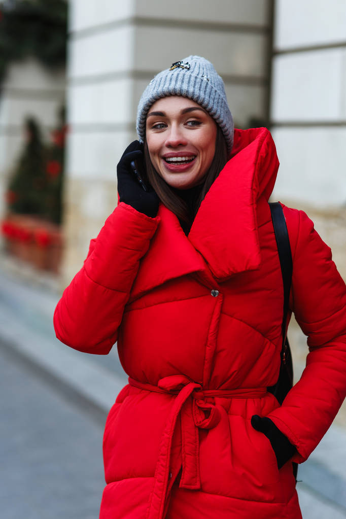 Portrait vertical de femme gaie sur fond de Noël Foire parler au téléphone. Femme en veste d'hiver rouge debout dans la rue le jour d'hiver. Noël vacances concept
 - Photo, image