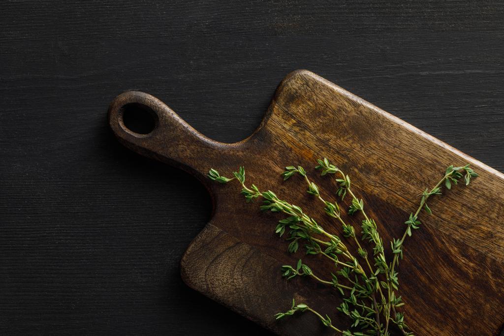 Top view of brown wooden cutting board with thyme twigs on dark surface - Photo, Image