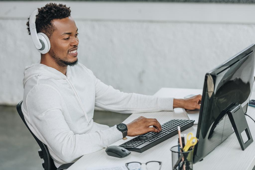 programador afroamericano feliz sentado en el lugar de trabajo en los auriculares
 - Foto, imagen