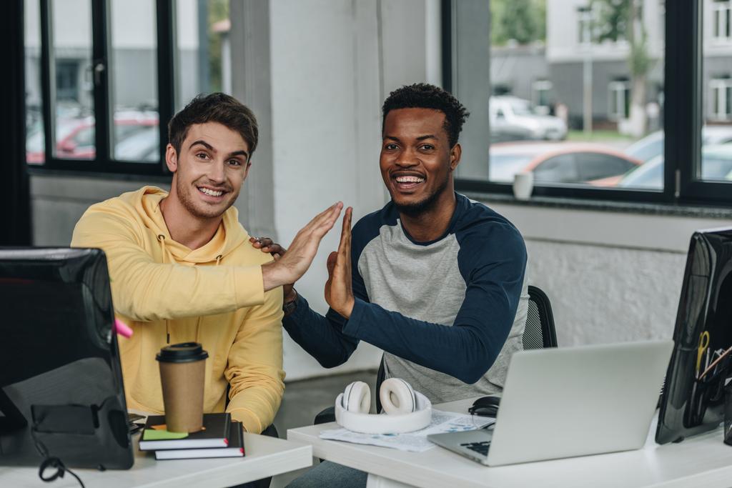 twee multiculturele programmeurs geven High Five en glimlachen op de camera in Office - Foto, afbeelding