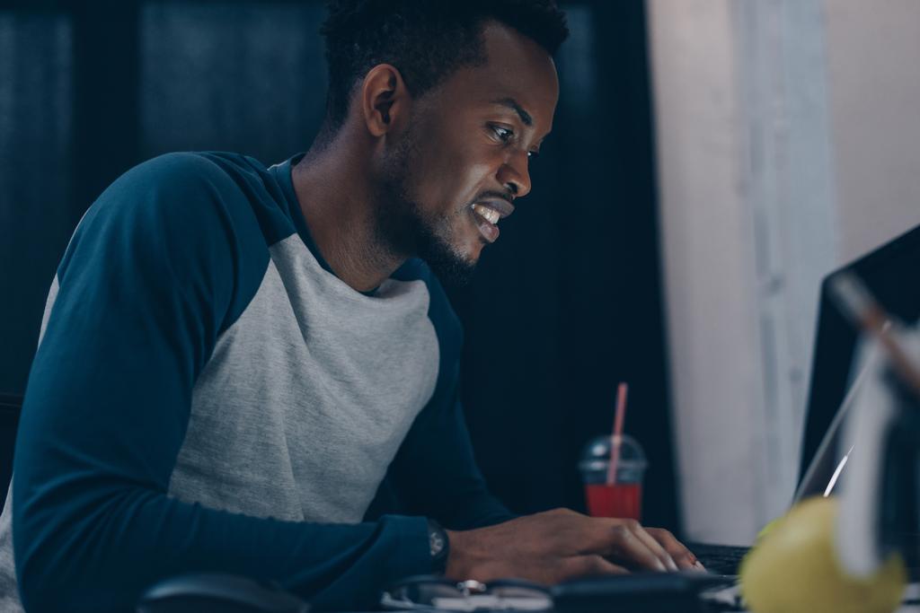 glimlachend Afro-Amerikaanse programmeur zittend op werkplek 's nachts - Foto, afbeelding