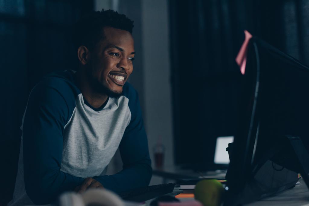 χαρούμενος Αφρικανός Αμερικανός προγραμματιστής χαμογελά κοιτάζοντας την οθόνη του υπολογιστή - Φωτογραφία, εικόνα