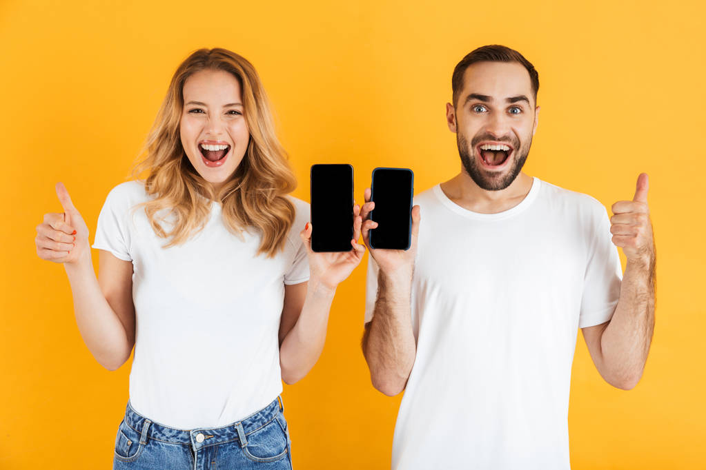 Kuva iloinen pari mies ja nainen näyttää peukalot ylös yhdessä pitäen matkapuhelimet
 - Valokuva, kuva