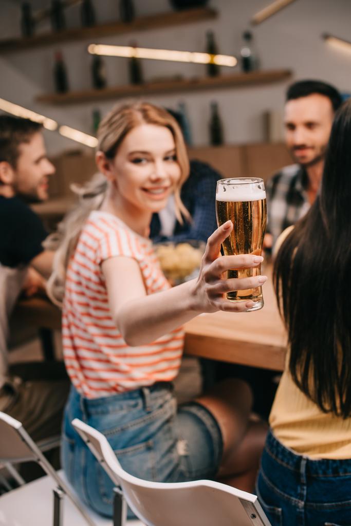 Selektywna koncentracja atrakcyjna młoda kobieta trzyma szklankę lekkiego piwa i patrząc na kamerę - Zdjęcie, obraz