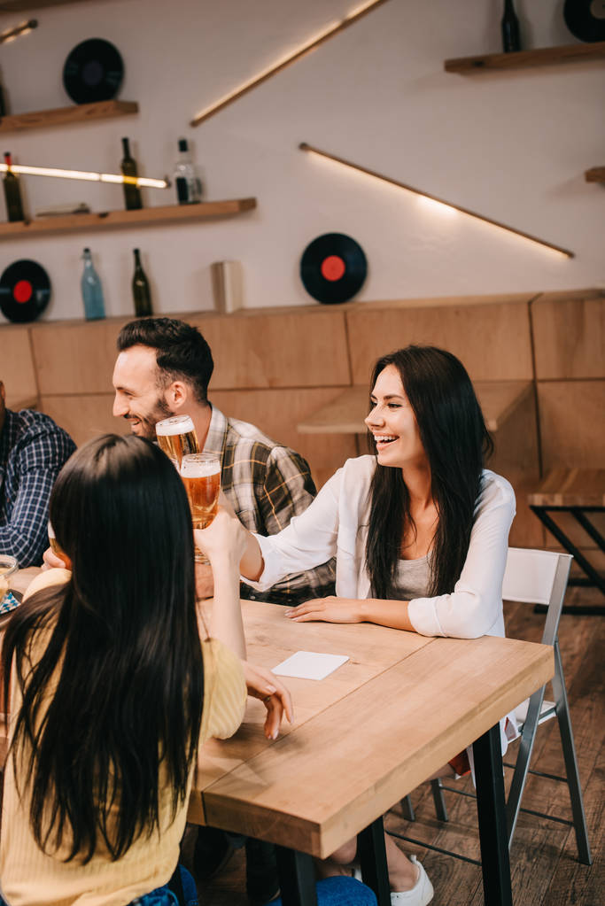 młode przyjaciółki klinujące kieliszki lekkiego piwa podczas spędzania czasu razem w pubu - Zdjęcie, obraz