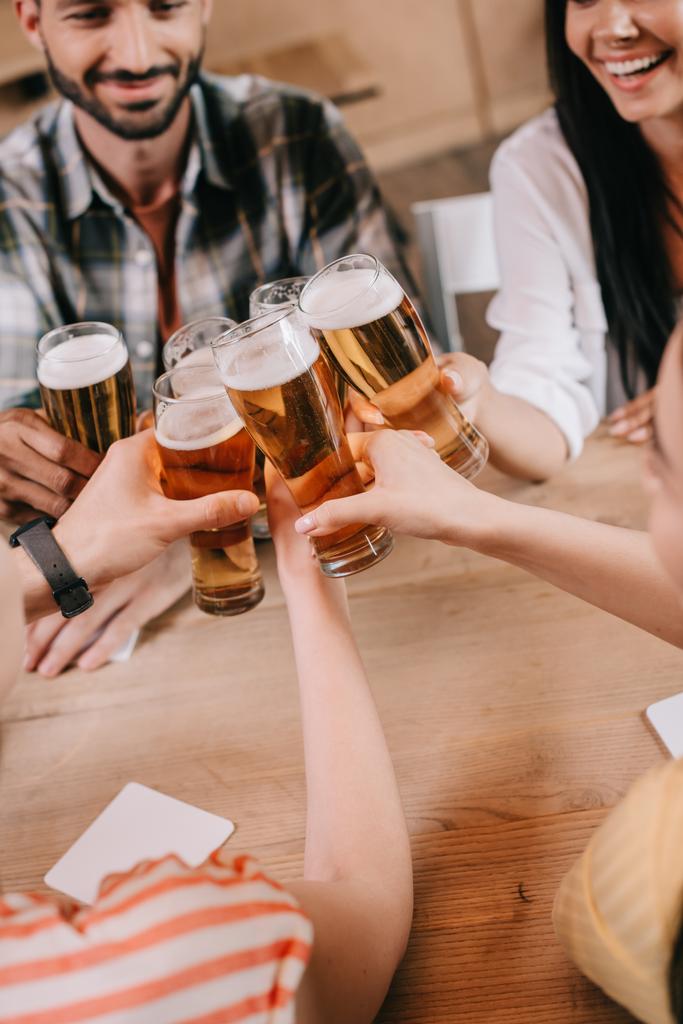 częściowy widok na wielokulturowe przyjaciółki klinujące kieliszki lekkiego piwa w pubie - Zdjęcie, obraz