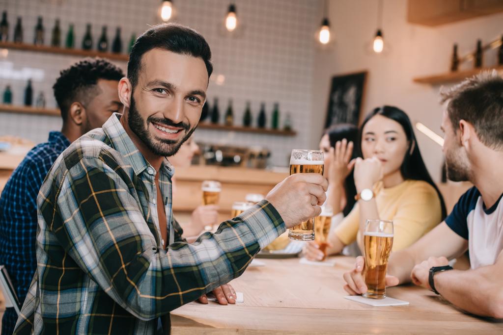 επιλεκτική εστίαση του χαμογελαστή άνθρωπο κοιτάζοντας την κάμερα, κρατώντας ένα ποτήρι μπύρας  - Φωτογραφία, εικόνα