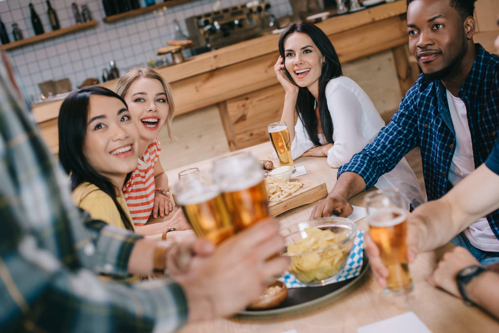 vista parziale dell'uomo che tiene bicchieri di birra leggera vicino agli amici multiculturali nel pub
 - Foto, immagini