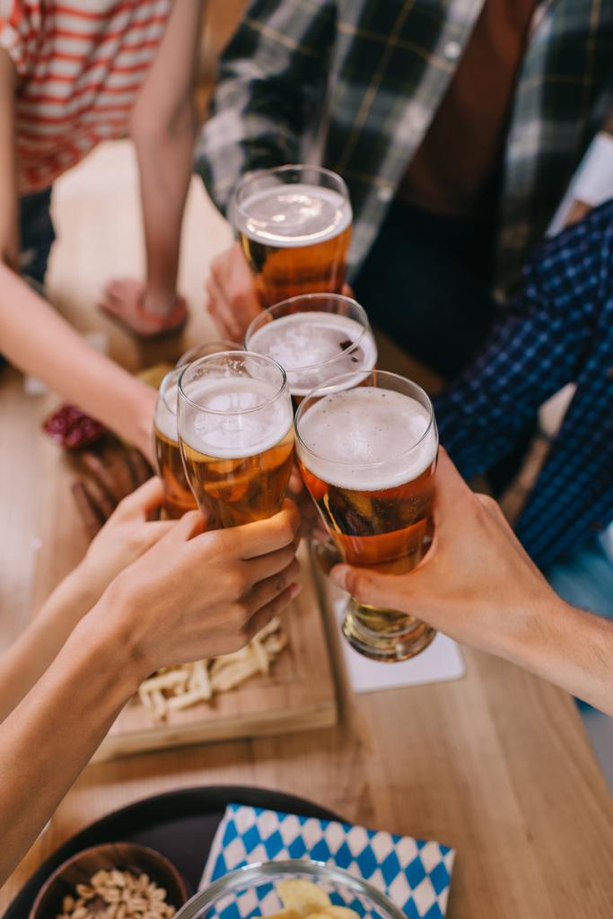 rajattu näkymä monikulttuurinen ystäviä clinking lasit kevyttä olutta pubissa
 - Valokuva, kuva