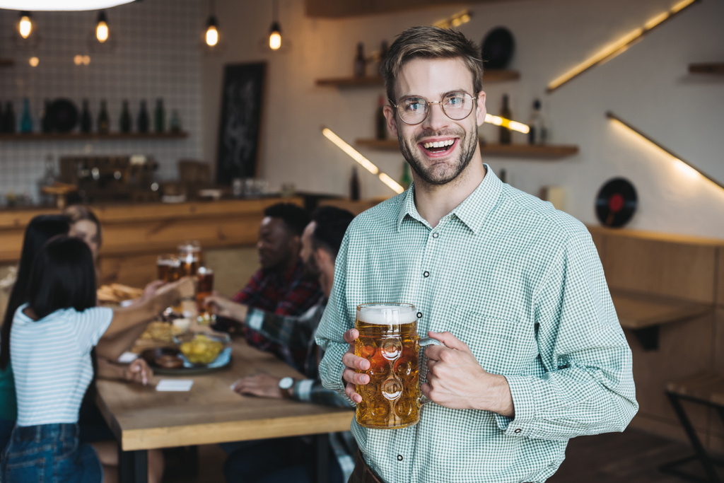  όμορφος νέος άντρας κρατώντας κούπα από ελαφριά μπύρα και χαμογελώντας στην κάμερα - Φωτογραφία, εικόνα