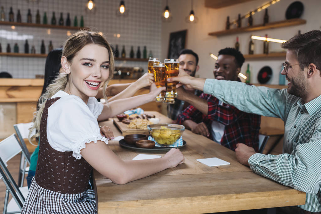 パブで10月の祭りを祝いながら、軽いビールのグラスを鳴らしている幸せな多文化の友人 - 写真・画像
