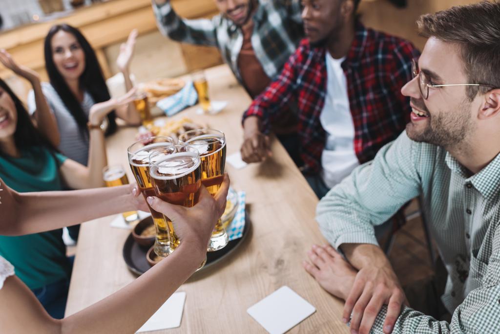 частичный вид официантки с бокалами светлого пива возле мультикультурных друзей
 - Фото, изображение