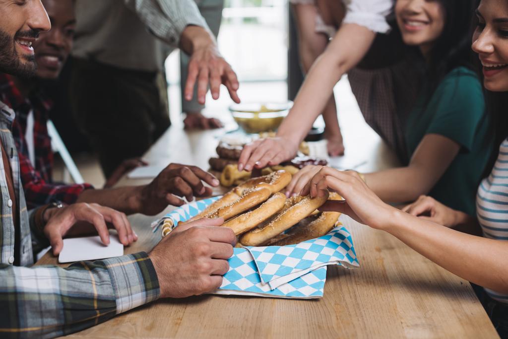bijgesneden uitzicht van multiculturele vrienden het nemen van smakelijke pretzels terwijl tijd samen doorbrengen in pub - Foto, afbeelding