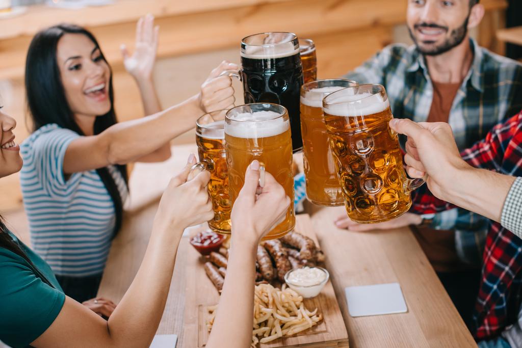 vrolijke vrienden klinkende mokken van bier tijdens het vieren van het Oktoberfest in pub - Foto, afbeelding