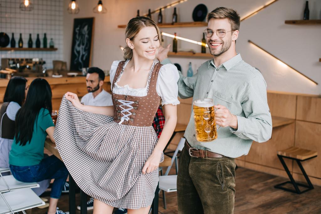 ευτυχισμένος άντρας και γυναίκα σε παραδοσιακές γερμανικές στολές που κρατούν κούπες μπύρας  - Φωτογραφία, εικόνα