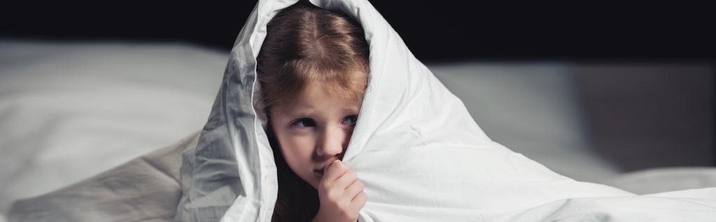 panoramic shot of scared child hiding under blanket isolated on black - Photo, Image