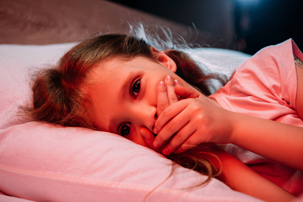 verängstigtes Kind blickt in Kamera, während es im Bett liegt und Schweigezeichen zeigt - Foto, Bild