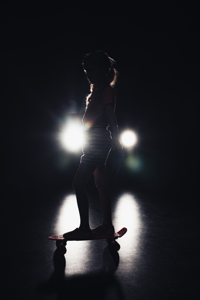 Kind reitet Penny Board in der Dunkelheit mit Beleuchtung der Scheinwerfer auf schwarzem Hintergrund - Foto, Bild