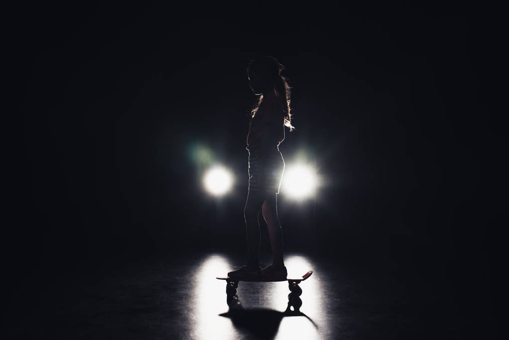 bambino in sella penny board nel buio con illuminazione dei fari su sfondo nero
 - Foto, immagini