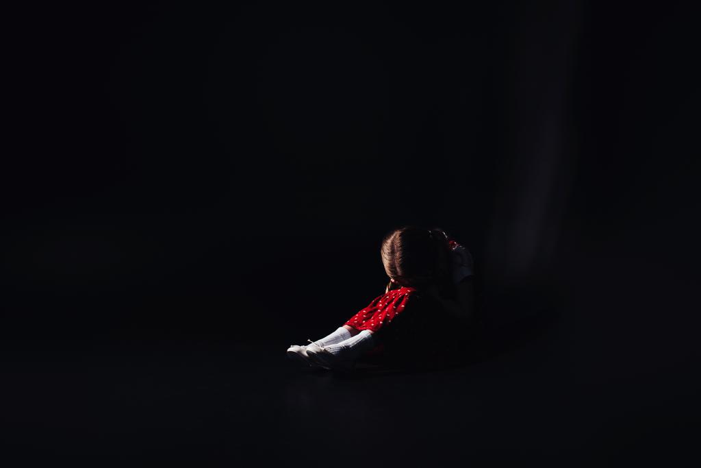 bambino depresso e spaventato seduto sul pavimento con la testa piegata isolata sul nero
 - Foto, immagini