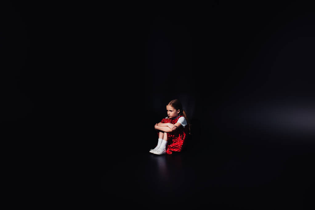 θλιμμένο, φοβισμένο παιδί που κάθεται στο πάτωμα απομονωμένος στο μαύρο - Φωτογραφία, εικόνα