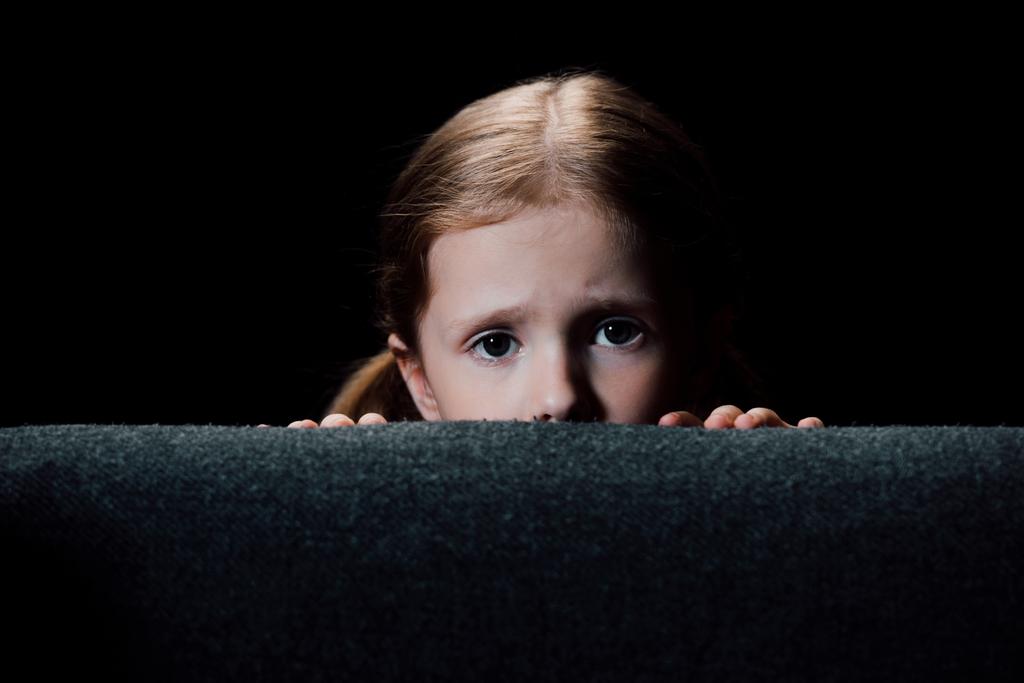 korkmuş çocuk koltuk arkasında gizleme ve siyah izole kamera bakıyor - Fotoğraf, Görsel