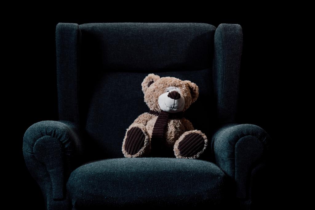 beige teddy bear in grey soft armchair isolated on black - Photo, Image