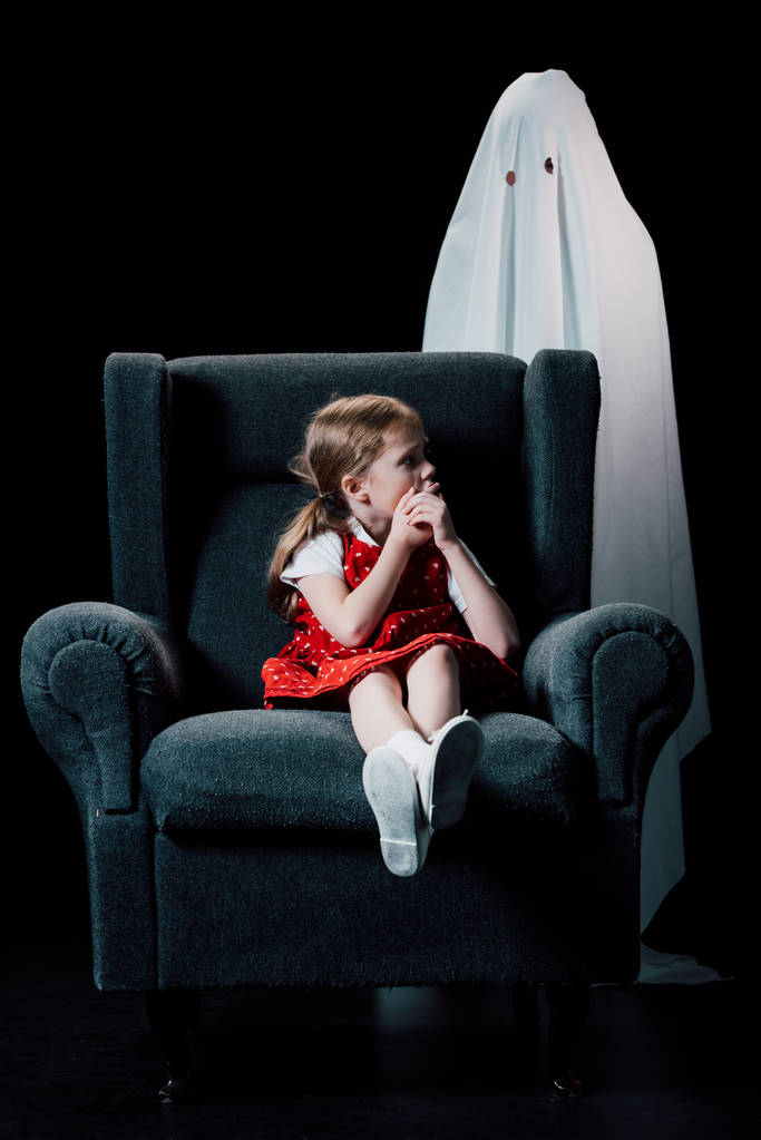 pelästynyt lapsi osoittaa hiljainen merkki lähellä valkoinen aave seisoo takana nojatuoli eristetty musta
 - Valokuva, kuva