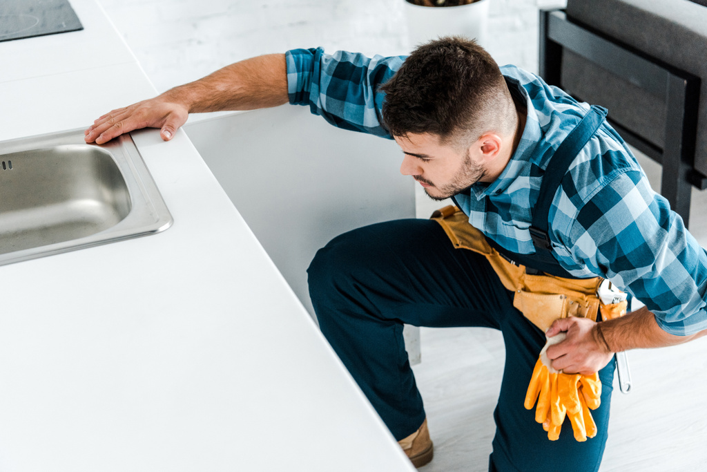 бородатый ремонтник с инструментальным ремнем сидит рядом с кухонным шкафом
  - Фото, изображение