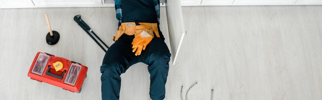 panoramic shot of handyman lying on floor near toolbox  - Photo, Image